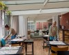 Dve čašníčky chystajú stoly v modernej reštaurácii s drevenou podlahou a veľkými oknami.