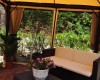 Pergola s pohovkou a kvetináčom obklopená zeleňou.
