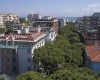 Pohľad na mestskú štvrť s hotelom Calypso a zelenými stromami, v pozadí je vidieť more.  
