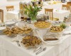 Stôl plný rôznych dezertov a pečiva vrátane croissantov a koláčov s kvetinovou dekoráciou v strede.