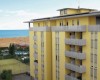 Žltá budova s balkónmi blízko pláže a tenisového kurtu.