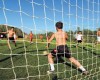 Deti hrajú futbal na trávnatom ihrisku za slnečného dňa.