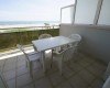 Balkón s výhľadom na pláž a more, vybavený štyrmi bielymi plastovými stoličkami a stolom.