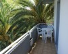 Úzky balkón s plastovým stolíkom a stoličkami, obklopený palmami.