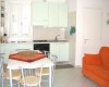 Malá kuchyňa s bielou linkou, jedálenský stôl so stoličkami a oranžová pohovka.