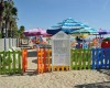 Detské ihrisko na pláži obklopené farebným plotom a slnečníkmi.