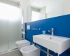 Moderná kúpeľňa s modrou stenou, umývadlom, toaletou a bidetom.