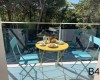 Dve modré stoličky a žltý stôl s raňajkami na balkóne s výhľadom do lesa.  