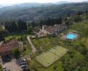Letecký pohľad na vidiecky rezort s bazénom, tenisovým kurtom a zelenými kopcami v pozadí.