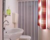 Kúpeľňa s umývadlom, toaletou a sprchovým závesom, ozdobená červenobielou záclonou.