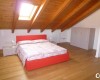 Spálňa v podkroví s drevenými trámami, červenou posteľou a bielym nábytkom.