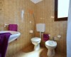 Kúpeľňa s umývadlom, toaletou a bidetom, vybavená fialovými uterákmi.