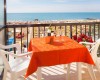 Zastrešený balkón s oranžovým obrusom, stoličkami a výhľadom na more a pláž.