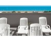 Biele plastové lehátka na terase s výhľadom na pláž a more.