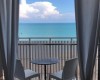 Výhľad z miestnosti na balkón s dvoma stoličkami a stolom, za ktorým je more a modrá obloha.