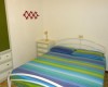 Spálňa s dúhovo pruhovanou prikrývkou na posteli, vedľa nej biely nočný stolík s lampičkou.