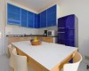 Kuchyňa s modrými skrinkami, stolom a fialovou chladničkou.