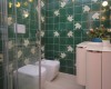 Kúpeľňa so zelenými dlaždicami s motívmi listov, bidetom a závesnou toaletou.