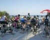 Skupina ľudí cvičí na stacionárnych bicykloch vonku pri mori.