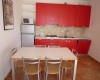 Kuchyň s červenými skrinkami, jedálenským stolom a štyrmi stoličkami.