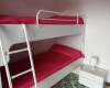 Poschodová posteľ s červenou posteľnou bielizňou a nočným stolíkom s lampou.
