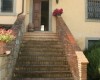 Kamenné schody vedúce k domu so žltou fasádou a kvetmi v kvetináčoch.