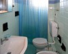 Kúpeľňa so svetlomodrými kachličkami, umývadlom, toaletou a bidetom, oddelená sprchovým závesom.