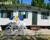 Mobilný dom s terasou, stolom a stoličkami pod modro-žltým slnečníkom.
