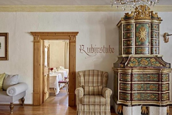 Rustikálna izba s kreslom, historickými kachľami a výhľadom do jedálne.