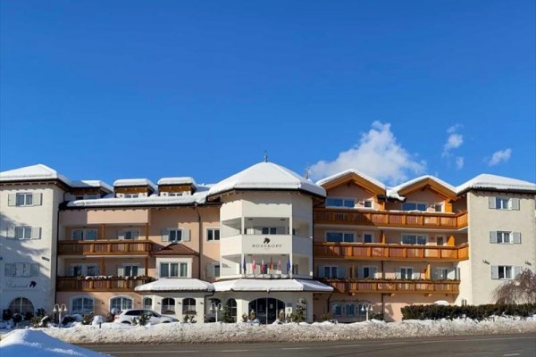 Veľký hotel s balkónmi počas zimného dňa na zasneženej ulici a modrou oblohou.