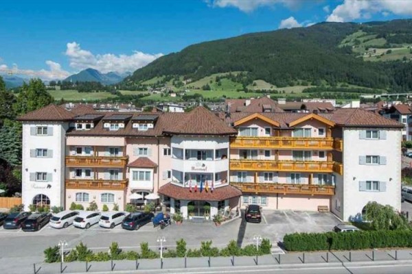 Hotel obklopený horami a zaparkovanými autami.