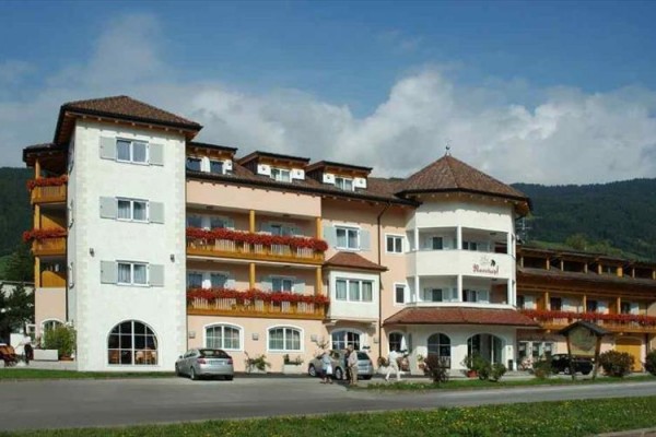 Veľký trojposchodový hotel so žltými a bielymi fasádami, balkónmi a zaparkovanými autami pred budovou.