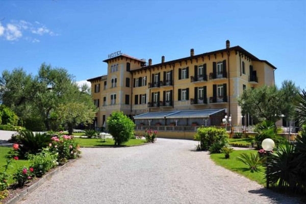 Veľký hotel uprostred upravenej záhrady s kvetmi a stromami.