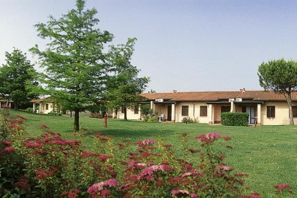 Trávnik s kríkmi a stromami pred radovými bungalovmi s terakotovou strechou.  