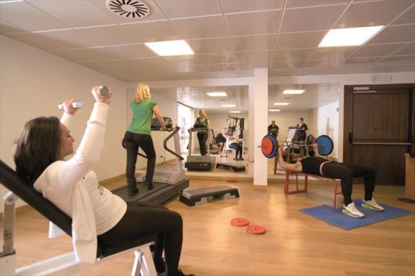 Ľudia cvičia v posilňovni s rôznym fitness vybavením.
