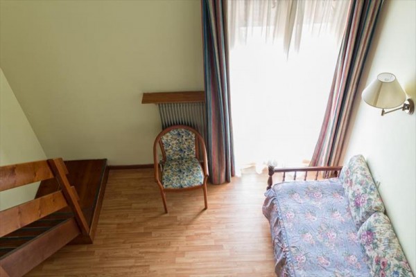 Izba s drevenou podlahou, stolom, stoličkou a pohovkou vedľa veľkého okna so záclonami.