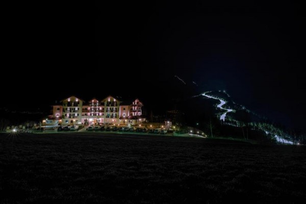 Osvetlený hotel v noci s osvetlenou horskou cestou v pozadí.