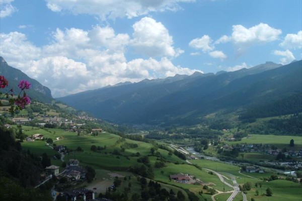 Údolie a mesto obklopené horami a sviežou zelenou krajinou pod modrou oblohou s obláčikmi.