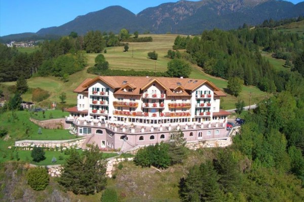 Veľký horský hotel obklopený zeleňou s horami v pozadí.