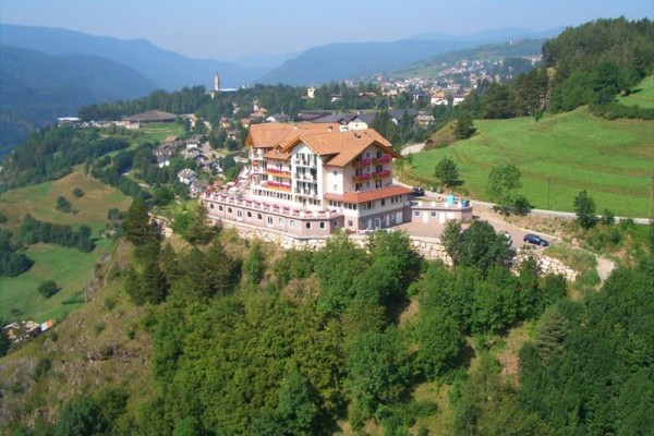 Hotel na vrchole kopca obklopený zelenými lúkami a lesmi.