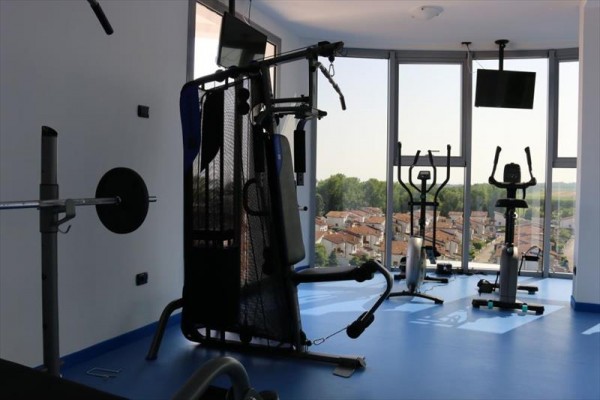 Posilňovňa s modernými fitness strojmi v miestnosti s veľkými oknami ponúkajúca výhľad na mesto.