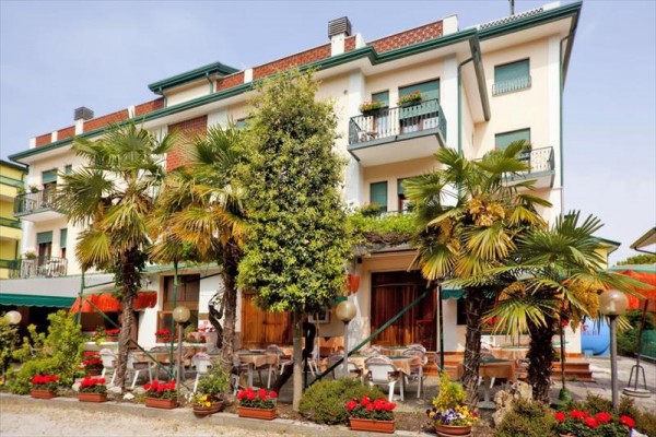Budova s balkónmi obklopená palmami a kvitnúcimi kvetmi.