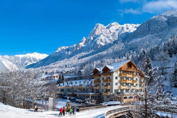 Snehom pokrytá horská krajina s hotelom a lyžiarmi na ceste.
