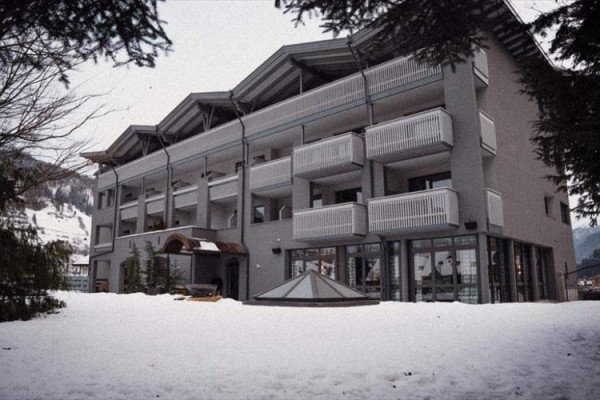 Trojposchodová budova s balkónmi obklopená zasneženou krajinou.