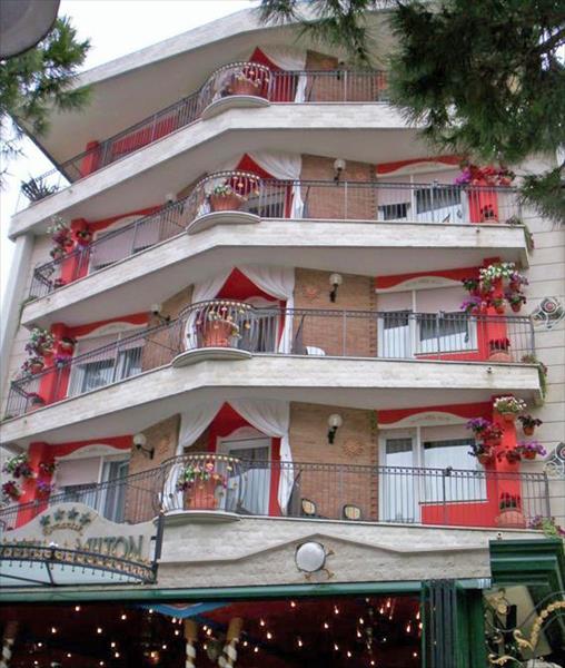 Päťposchodová budova s balkónmi ozdobenými kvetmi a červenobielymi závesmi.