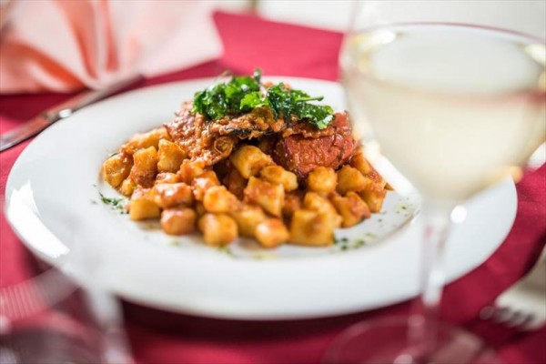 Tanier gnocchi s paradajkovou omáčkou a bylinkami na stole s bielym vínom.