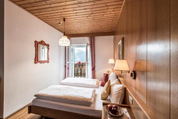 Tradičná útulná spálňa s dreveným stropom, dvojlôžkom a výhľadom na balkón s horskou scenériou vonku.