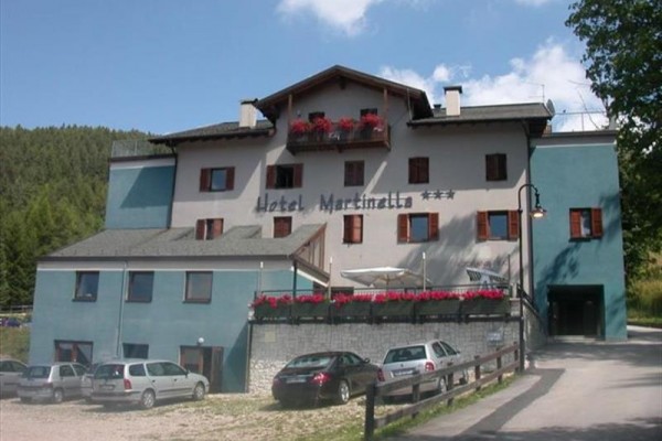 Trojpodlažný hotel s balkónmi ozdobenými kvetmi a niekoľkými zaparkovanými autami pred budovou.