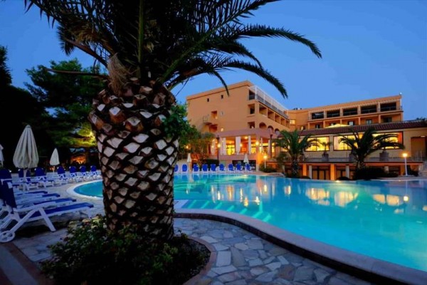 Večerný pohľad na hotel s bazénom a palmami.