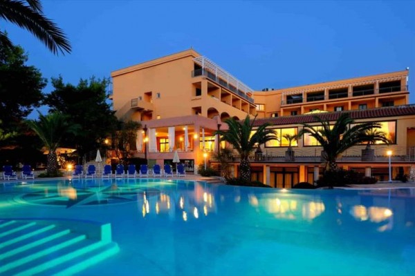 Moderný hotel pri osvetlenom bazéne s palmami za súmraku.
